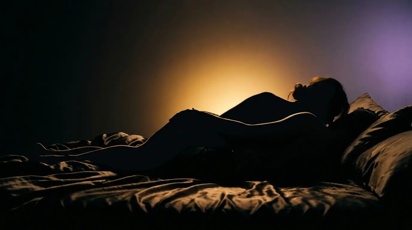 Artistic warm amber backlit silhouette of couple in spooning position on luxurious bed with dark silk sheets