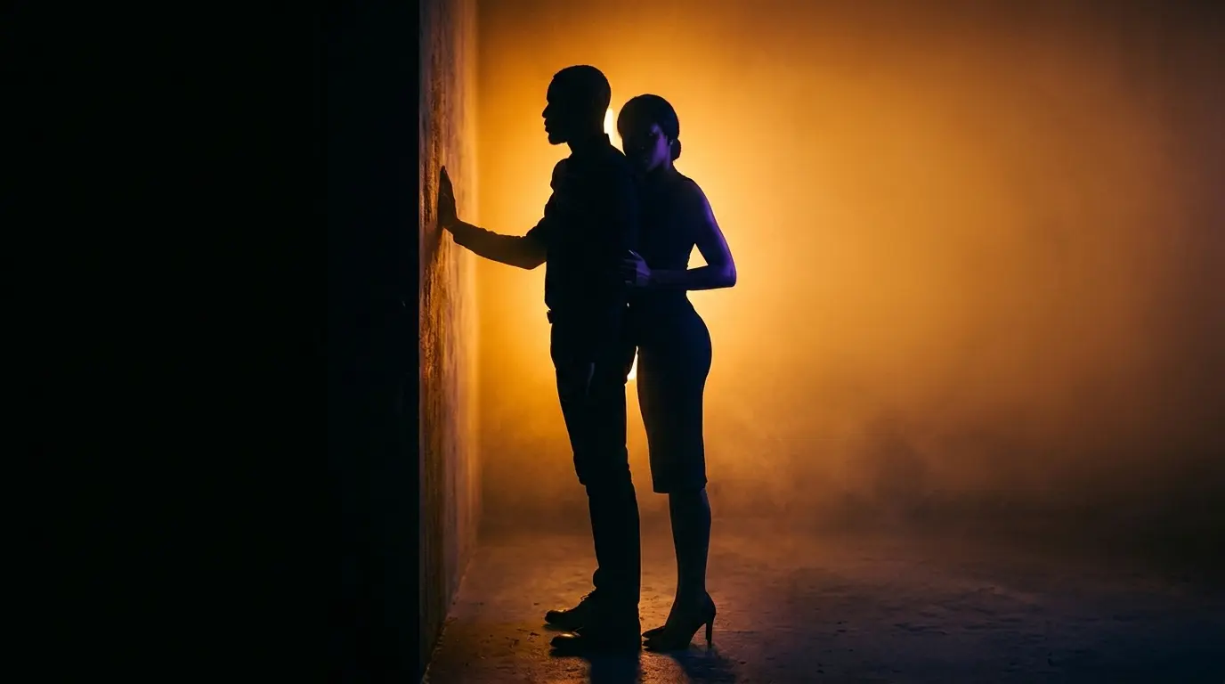 Dramatic vertical silhouette of standing couple with the giver behind, warm amber rim lighting and dark moody atmosphere